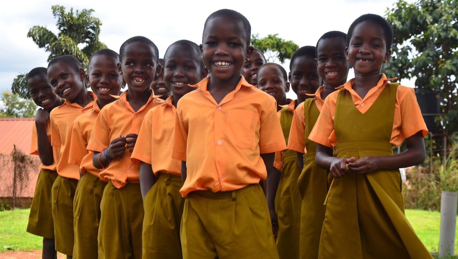Group of smiling school children in uniform outdoors in a rural setting.